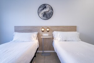 Ein Hotelzimmer mit zwei Einzelbetten, einer runden Wanduhr und einem kleinen Tisch mit zwei Wandleuchten.