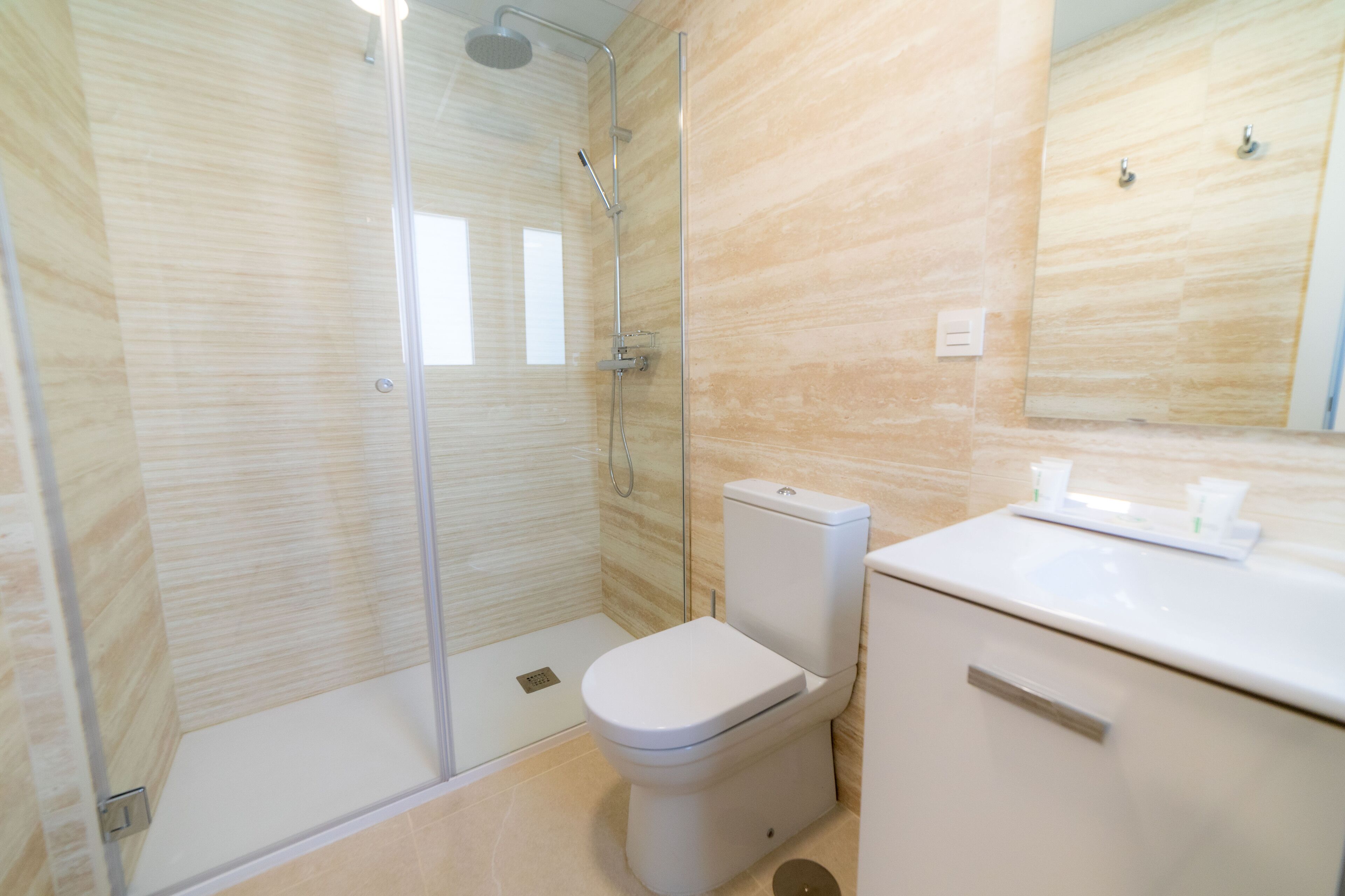 A modern bathroom with a glass-enclosed shower, a toilet, and a sink with a mirror above.