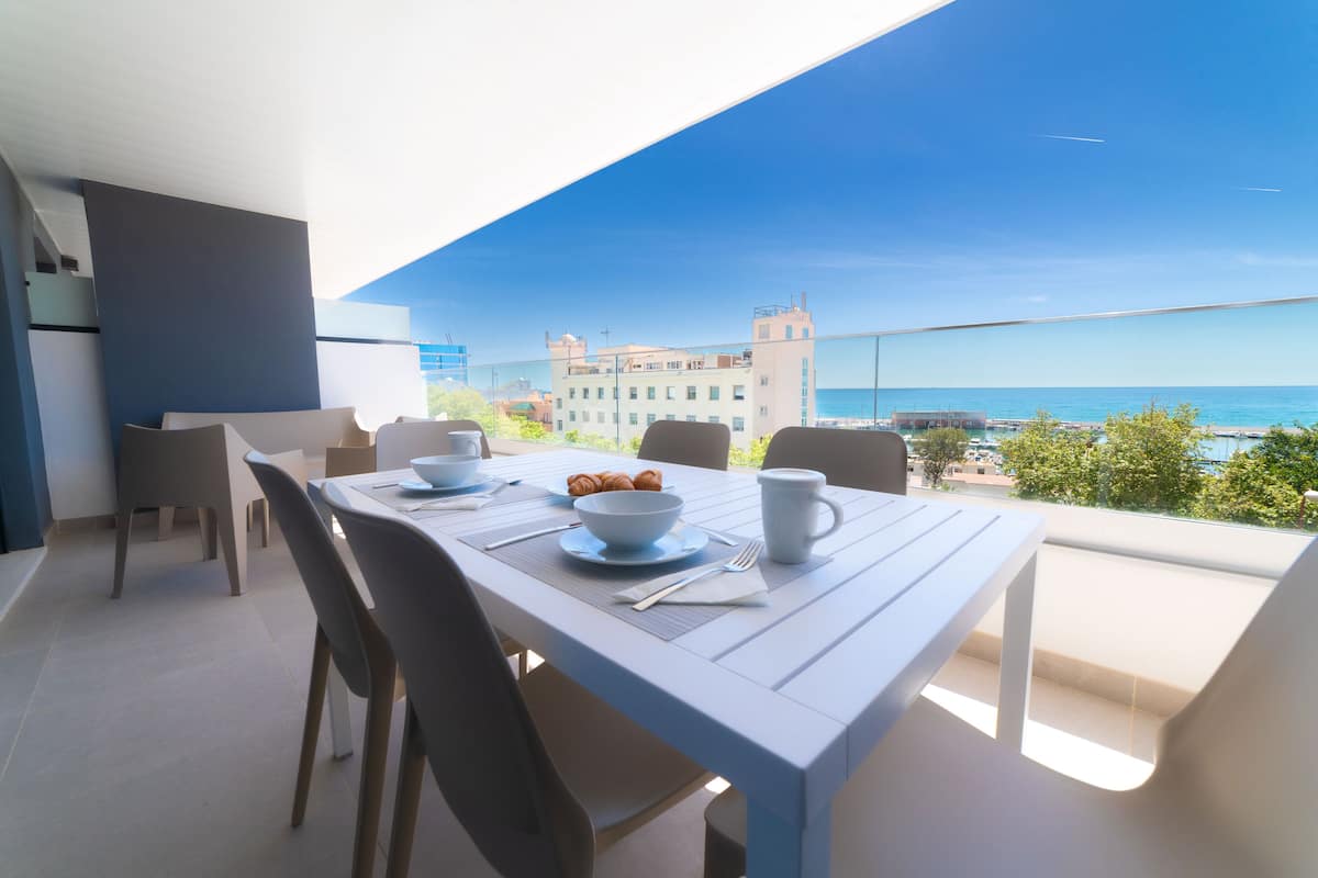 A dining area with a table set for two, overlooking a scenic view of the sea and buildings.