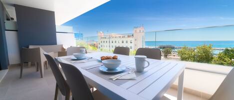 A dining area with a table set for two, overlooking a scenic view of the sea and buildings.