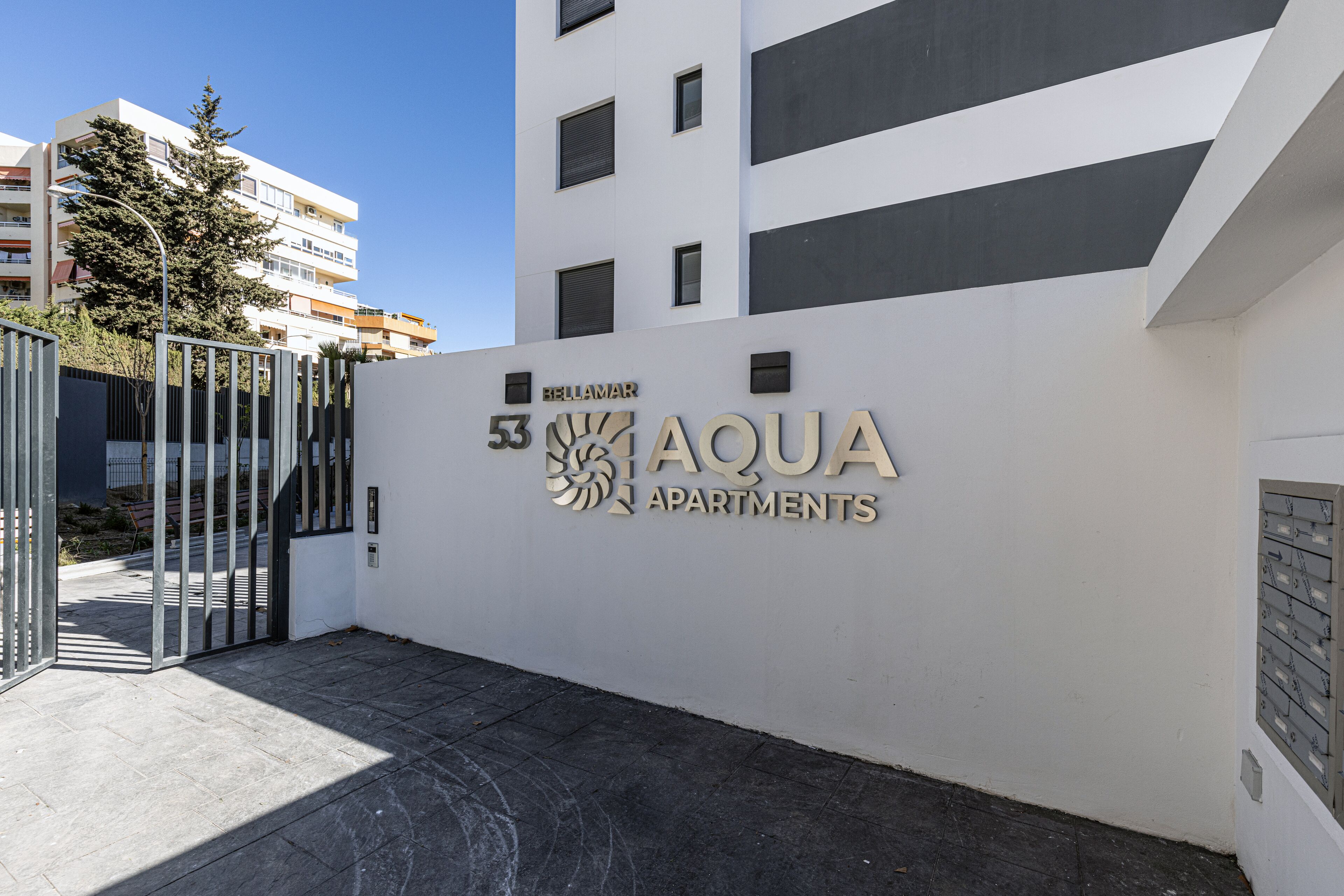 Une entrée d’immeuble avec une enseigne indiquant « AQUA APARTMENTS » et un portail.