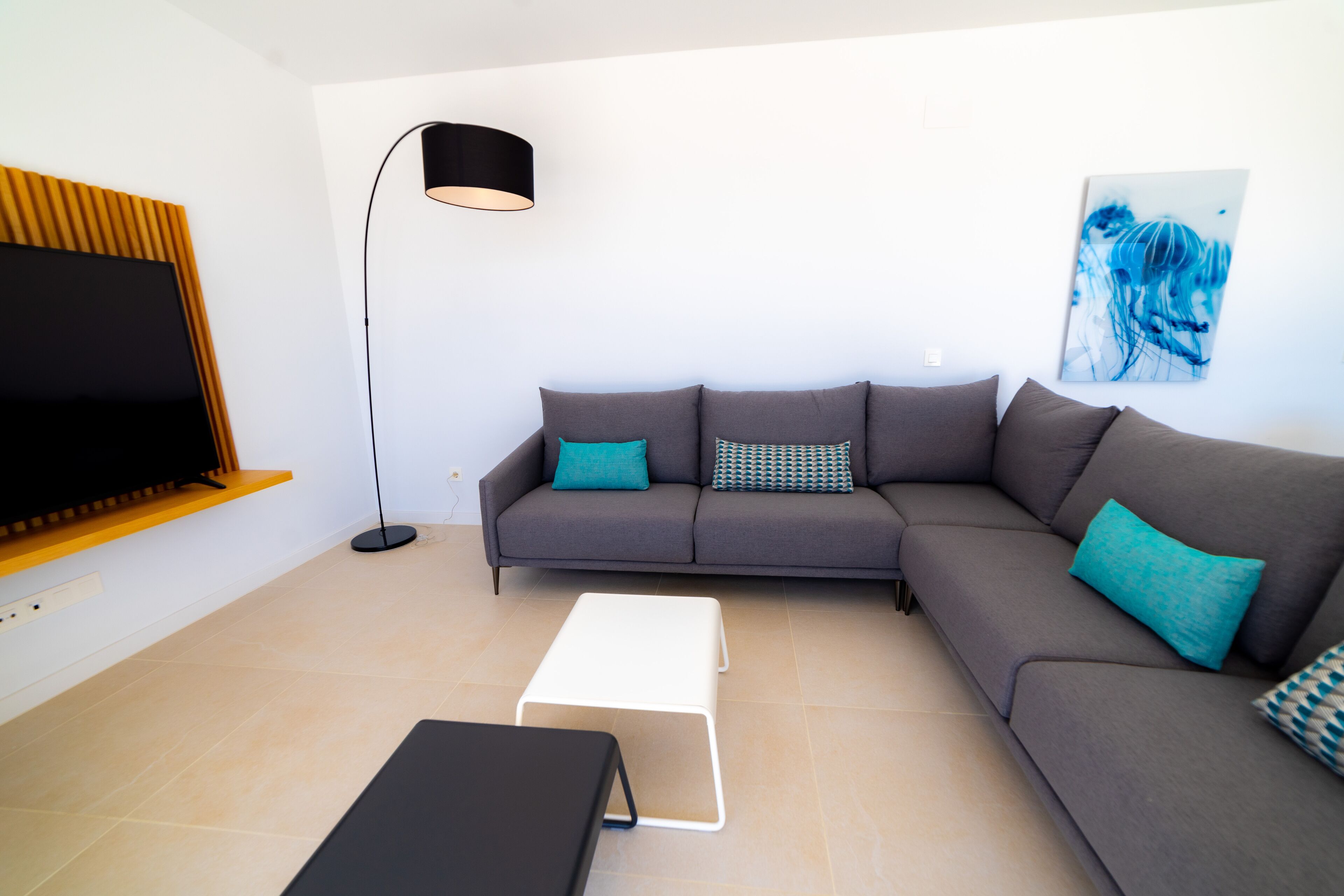 Un salon moderne avec un canapé d’angle, un téléviseur à écran plat, une lampe sur pied et une table basse.