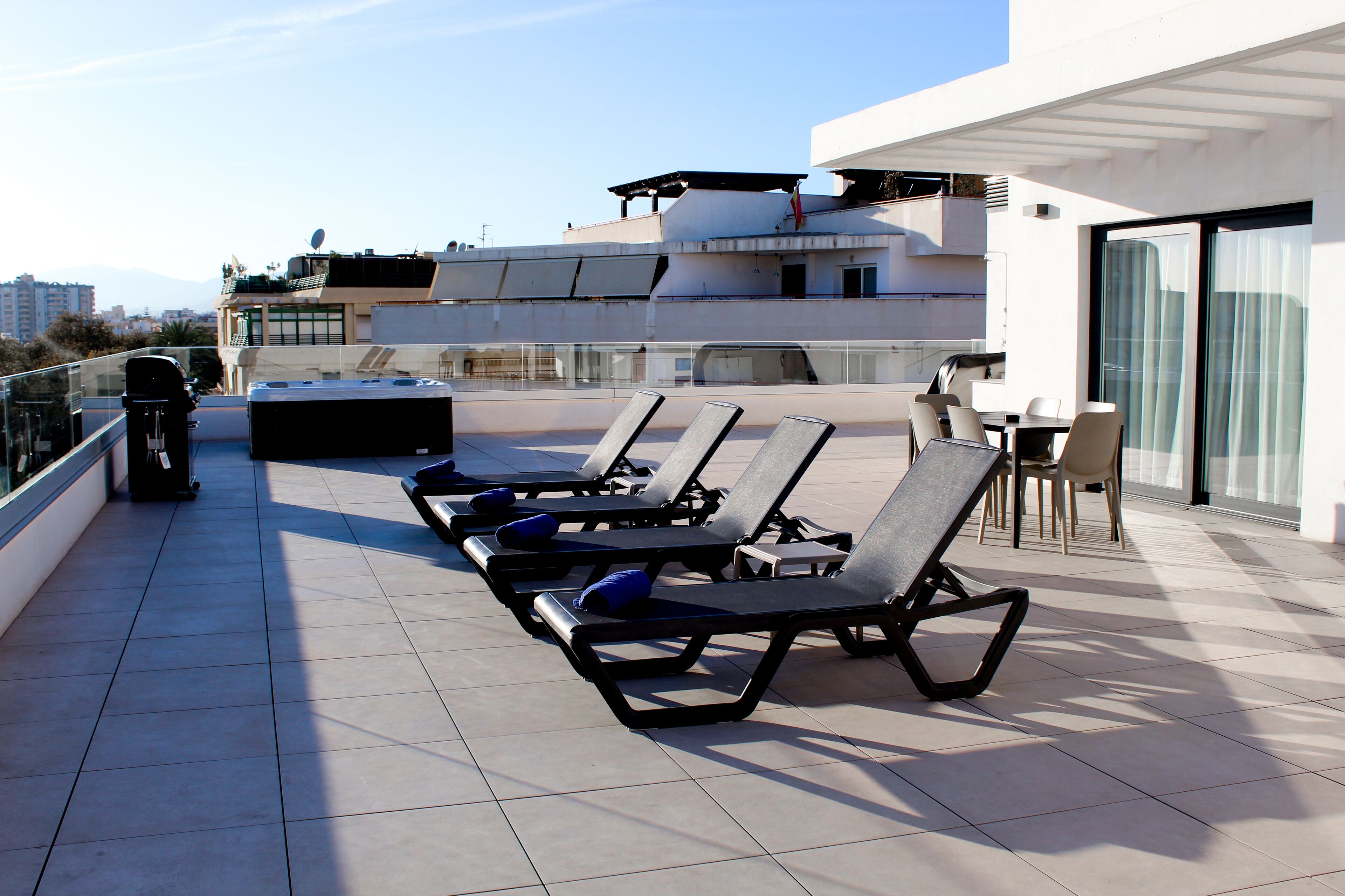 A rooftop terrace with sun loungers, a table, and chairs.