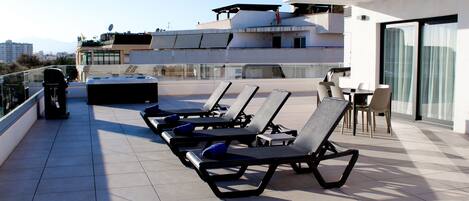 A rooftop terrace with sun loungers, a table, and chairs.