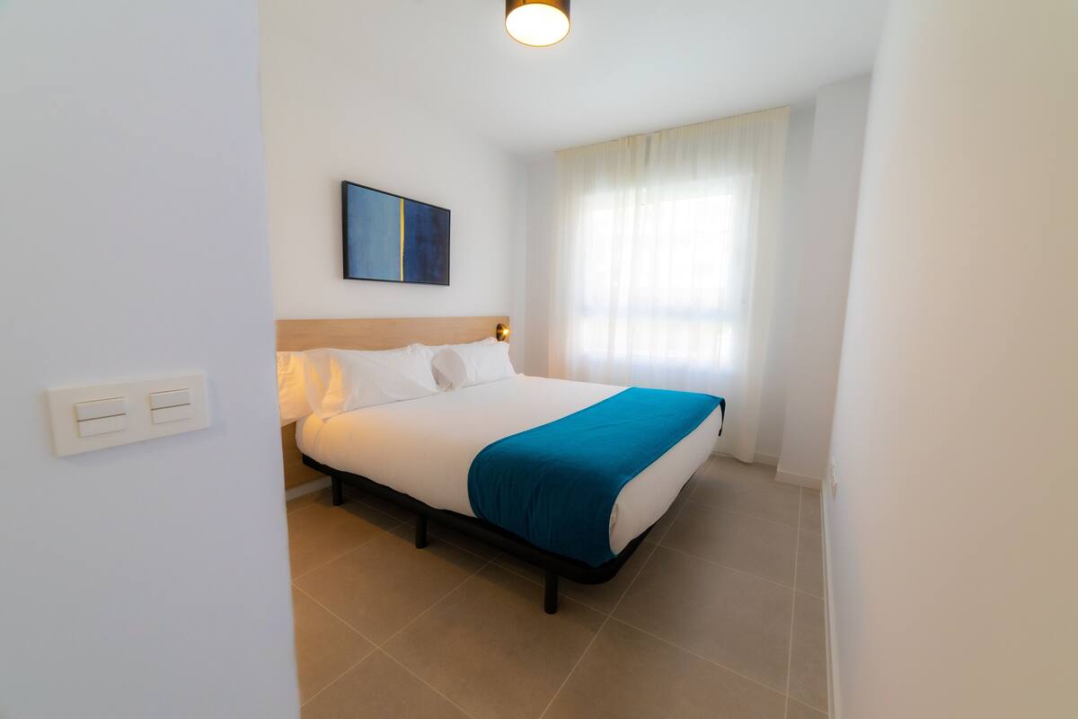 A hotel room with a bed, a painting on the wall, and a window with curtains.