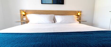 A neatly made bed with a blue blanket, a wooden headboard, and two bedside lamps.