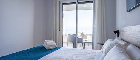 A hotel room with a bed, a blue towel, a white headboard, and a view of the balcony and cityscape.