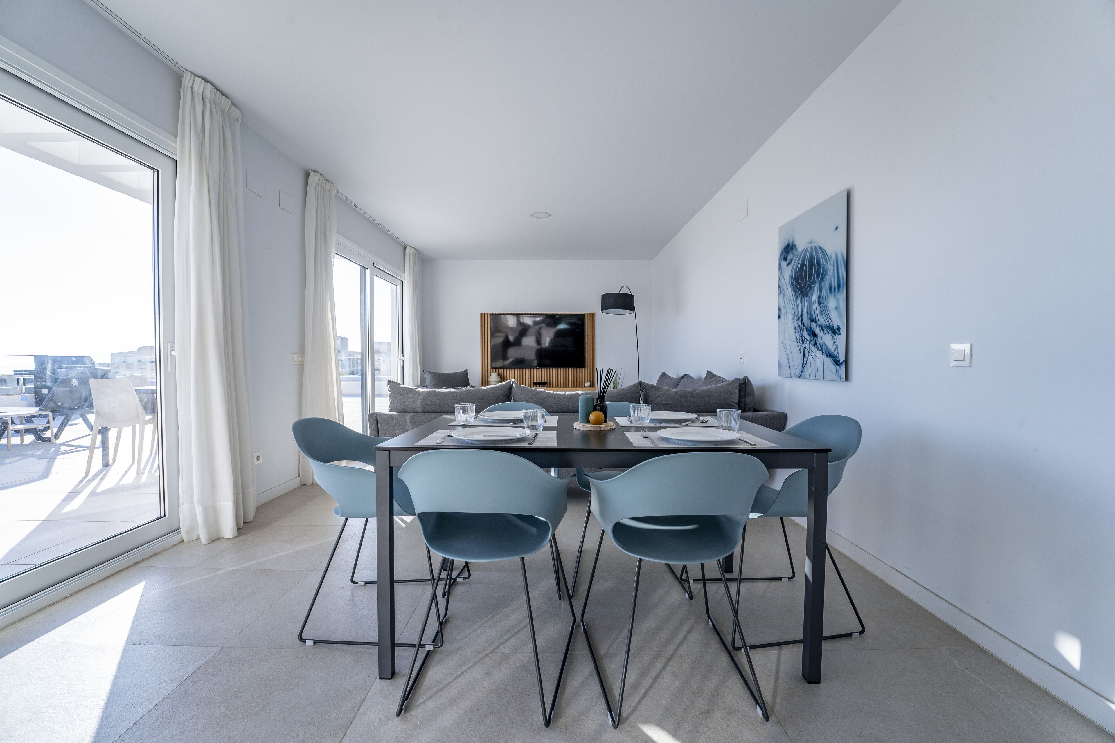 Un espace de salle à manger moderne, doté d’une grande table, de quatre chaises et offrant une vue sur la ville grâce à de larges fenêtres.