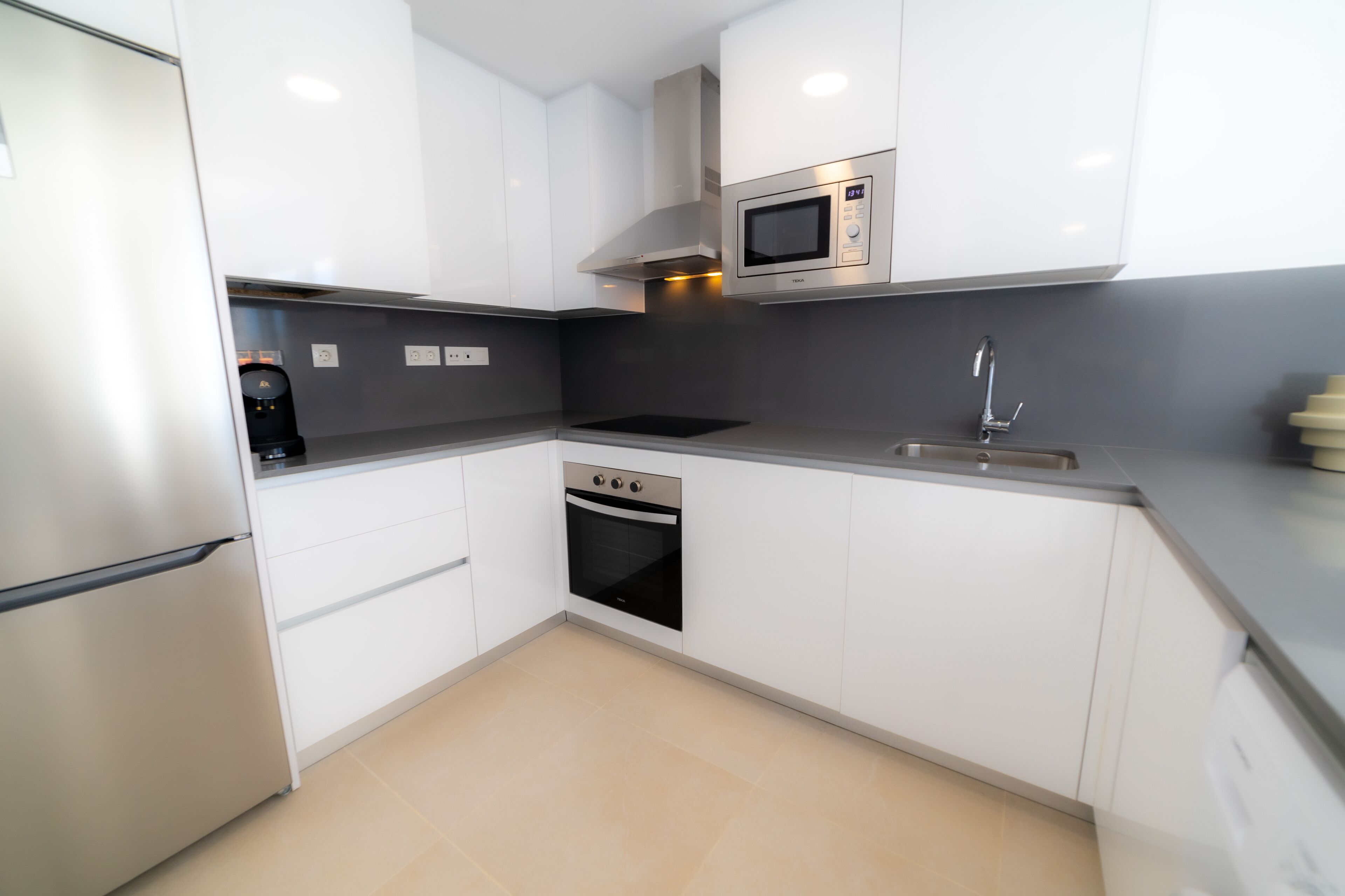 A modern kitchen with white cabinets, a built-in microwave, a stainless steel oven, and a sink.