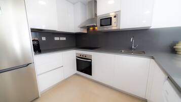 Una cuina moderna amb armaris blancs, un microones integrat, un forn d'acer inoxidable i un rentaplat.
