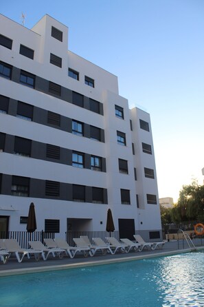 A modern hotel with a pool, multiple floors, and a row of sun loungers along the poolside. - Aqua Apartments Bellamar Marbella (Marbella)