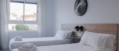 A hotel room with two beds, a large window, a wall-mounted artwork, and a nightstand with a lamp.