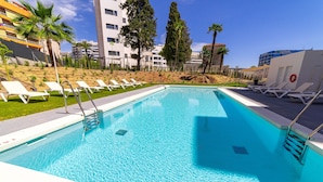 Une piscine dotée de chaises longues et d’une bouée de sauvetage, entourée d’immeubles et de palmiers.