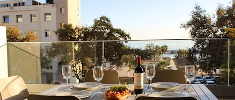 Une table à manger dressée avec des assiettes, des couverts et des verres à vin, ainsi qu’une bouteille de vin et une assiette de raisins.
