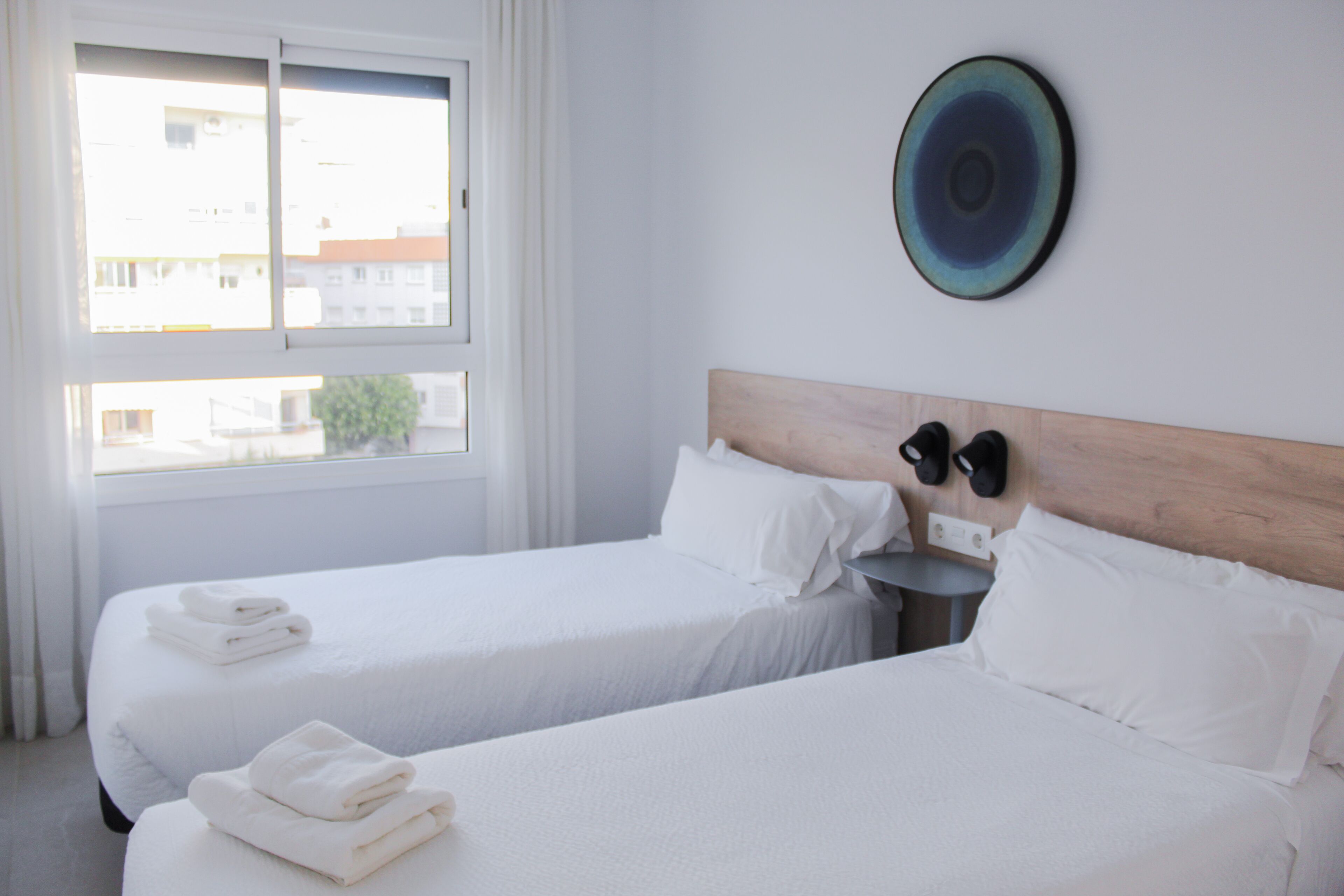 A hotel room with two beds, white bedding, a round wall decoration, and a window with curtains.