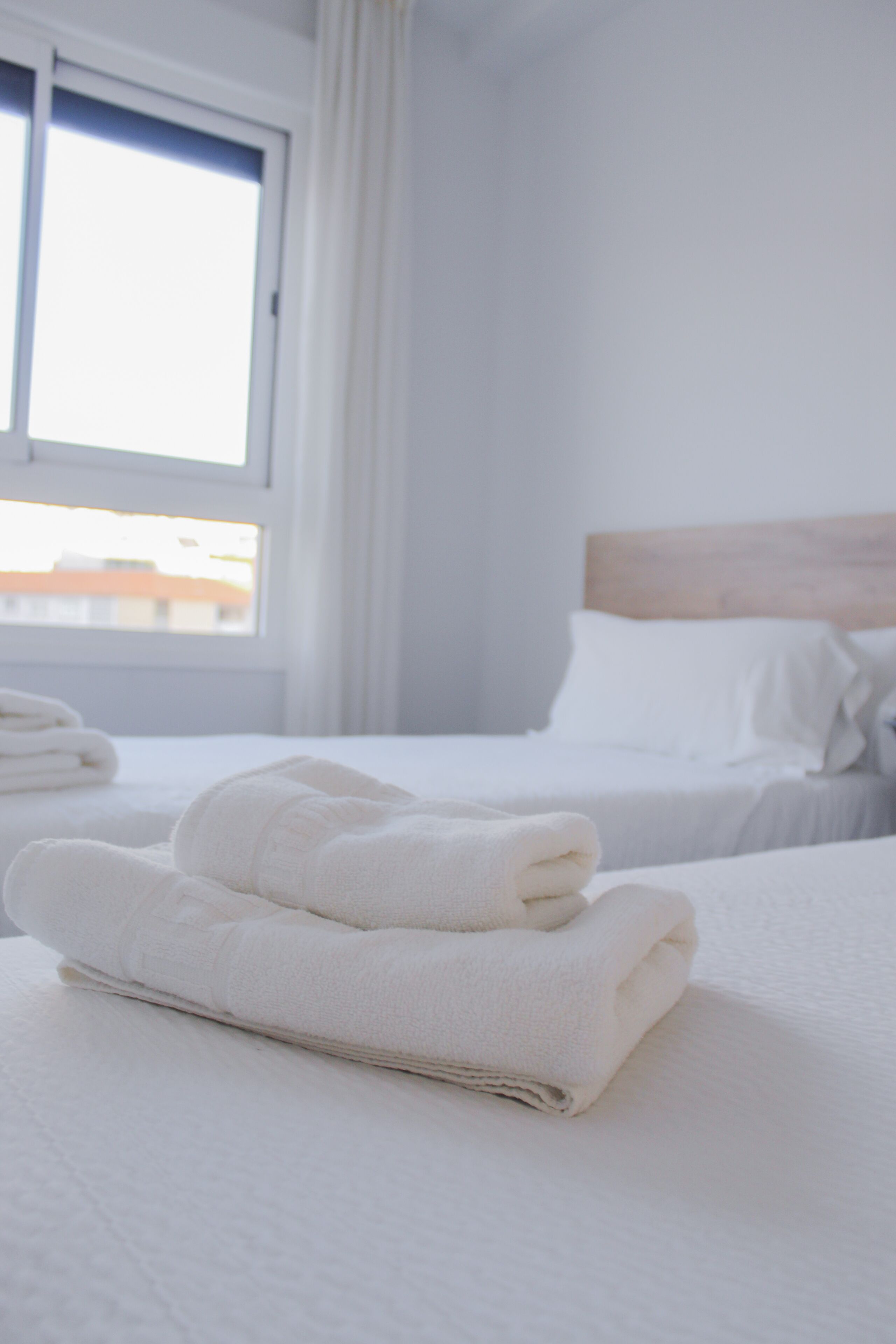 A hotel room with two beds, white linens, and a window with curtains.