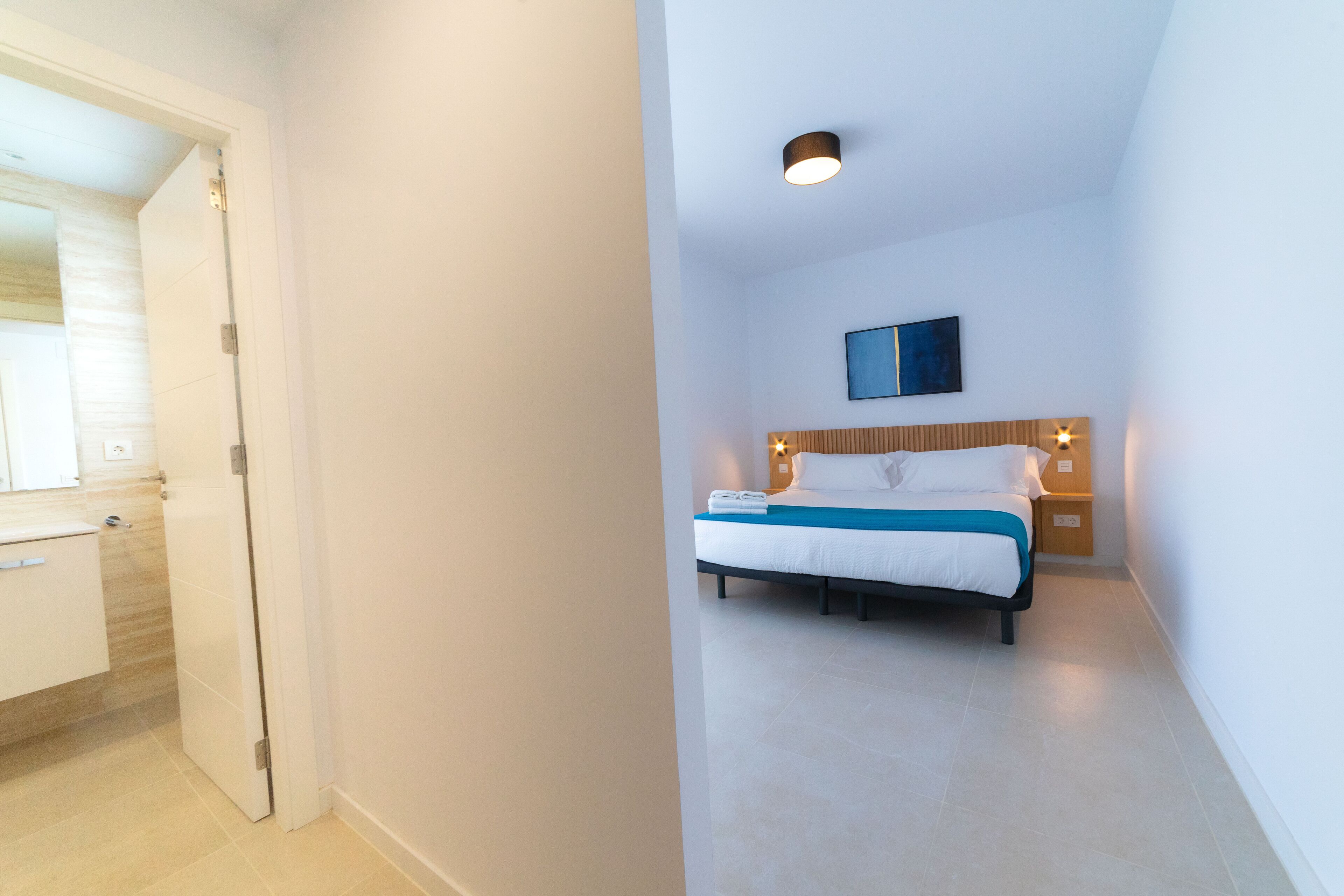 A hotel room with a bed, a nightstand, a wall-mounted TV, and a door leading to a bathroom.