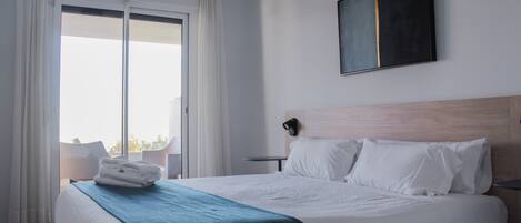 Et hotelværelse med en stor seng, udsigt til naturen gennem en skydedør, et billedværk på væggen og et lille bord med en stol.