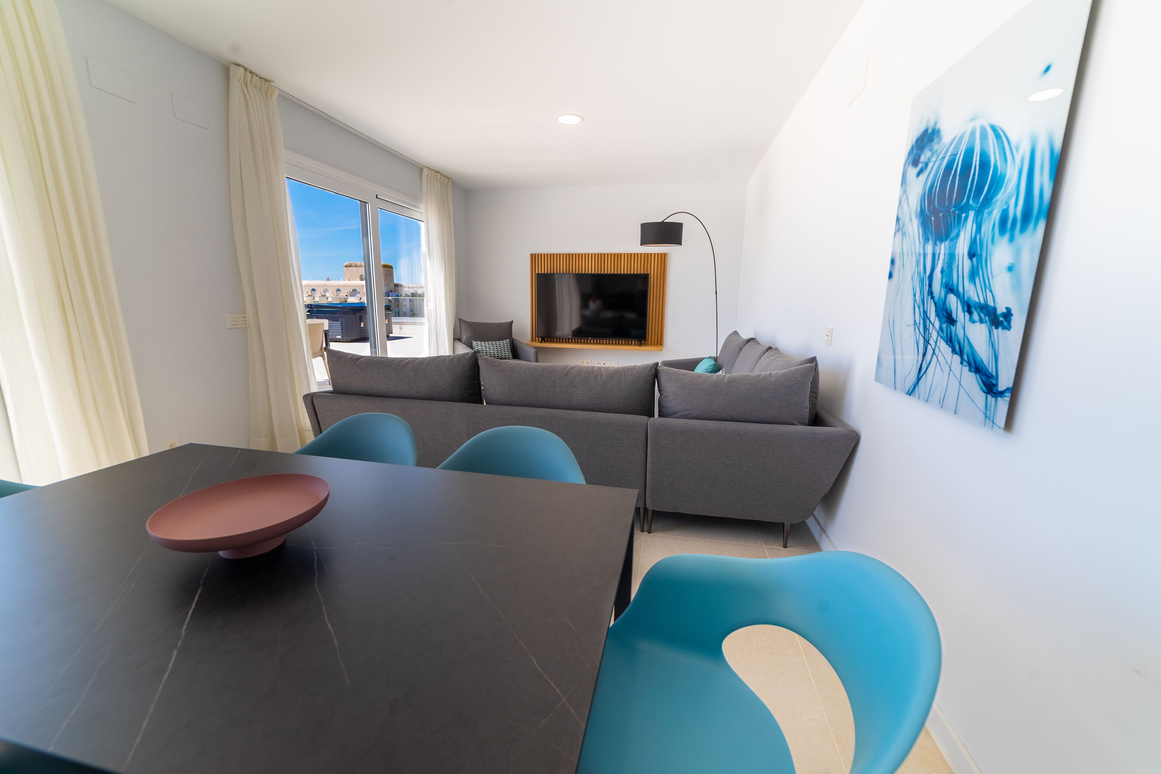 Una sala moderna con un conjunto de sofás, una mesa de comedor con sillas, un televisor de pantalla plana montado en la pared y un cuadro abstracto grande.