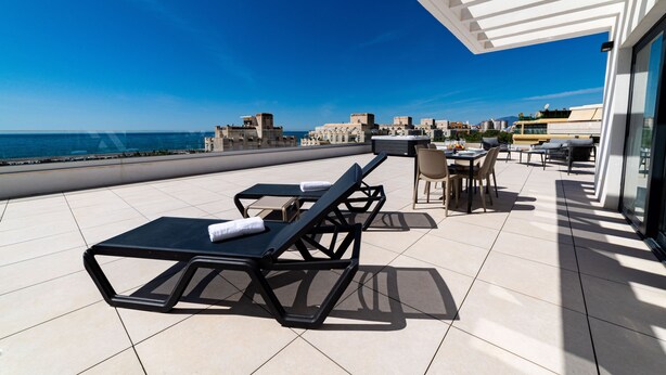 Une terrasse sur le toit, dotée de chaises longues et d’un espace repas offrant une vue sur la mer.