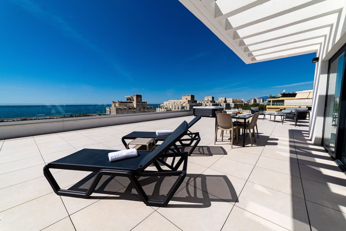 A rooftop terrace with lounge chairs and a dining area overlooking the sea.