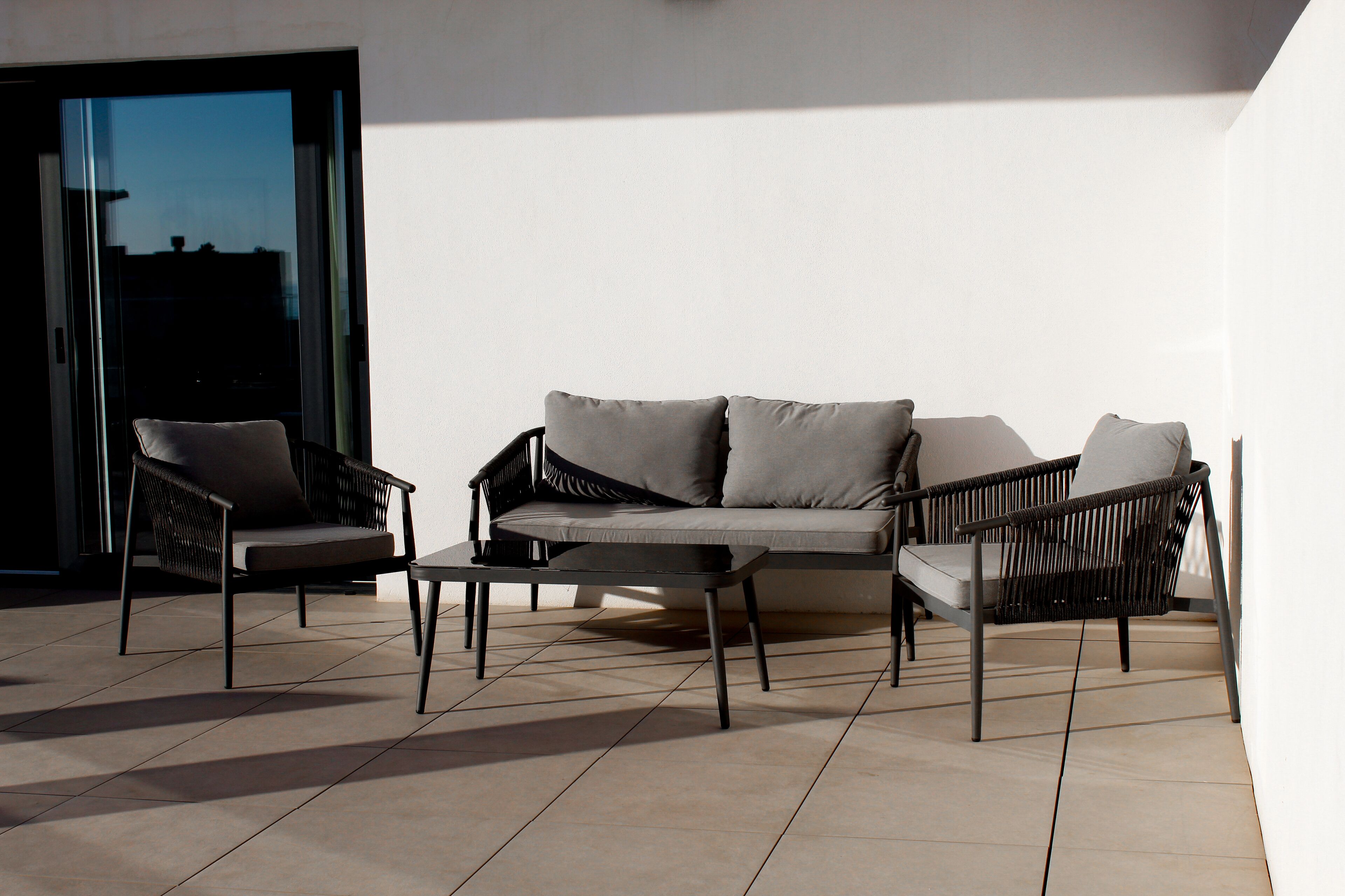 An outdoor seating area with a sofa and two chairs, a coffee table, and a glass door leading to the interior.