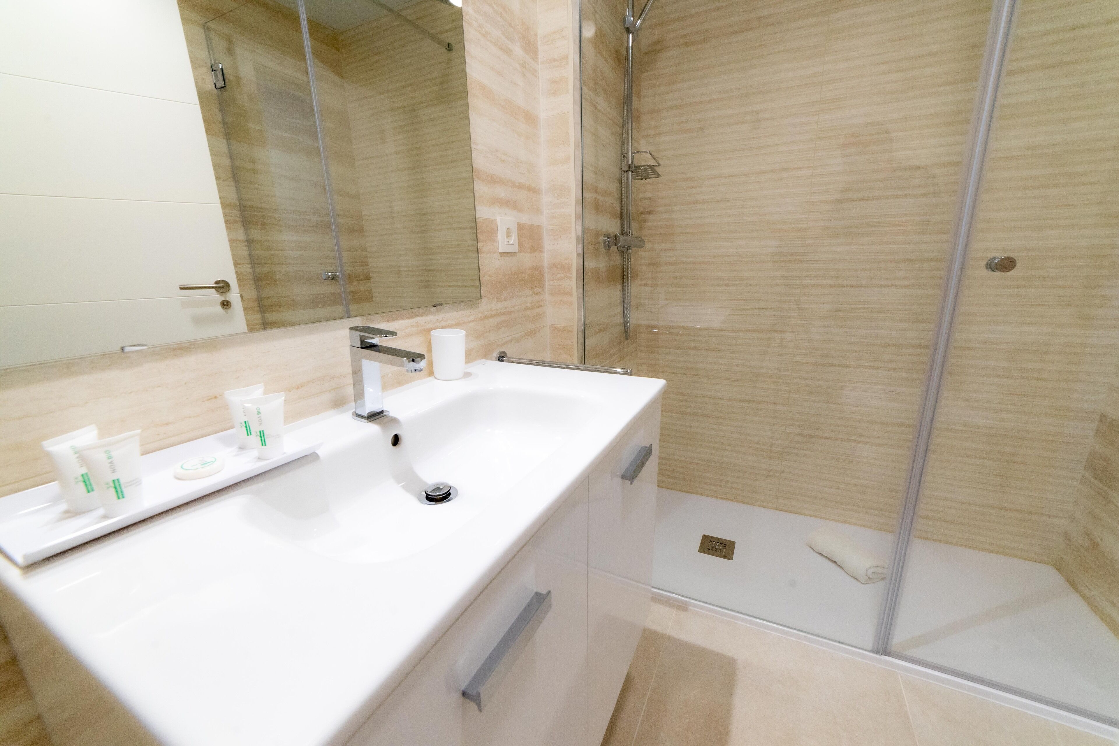Ein modernes Badezimmer mit Waschbecken, Spiegel und Duschkabine in Weiß.
