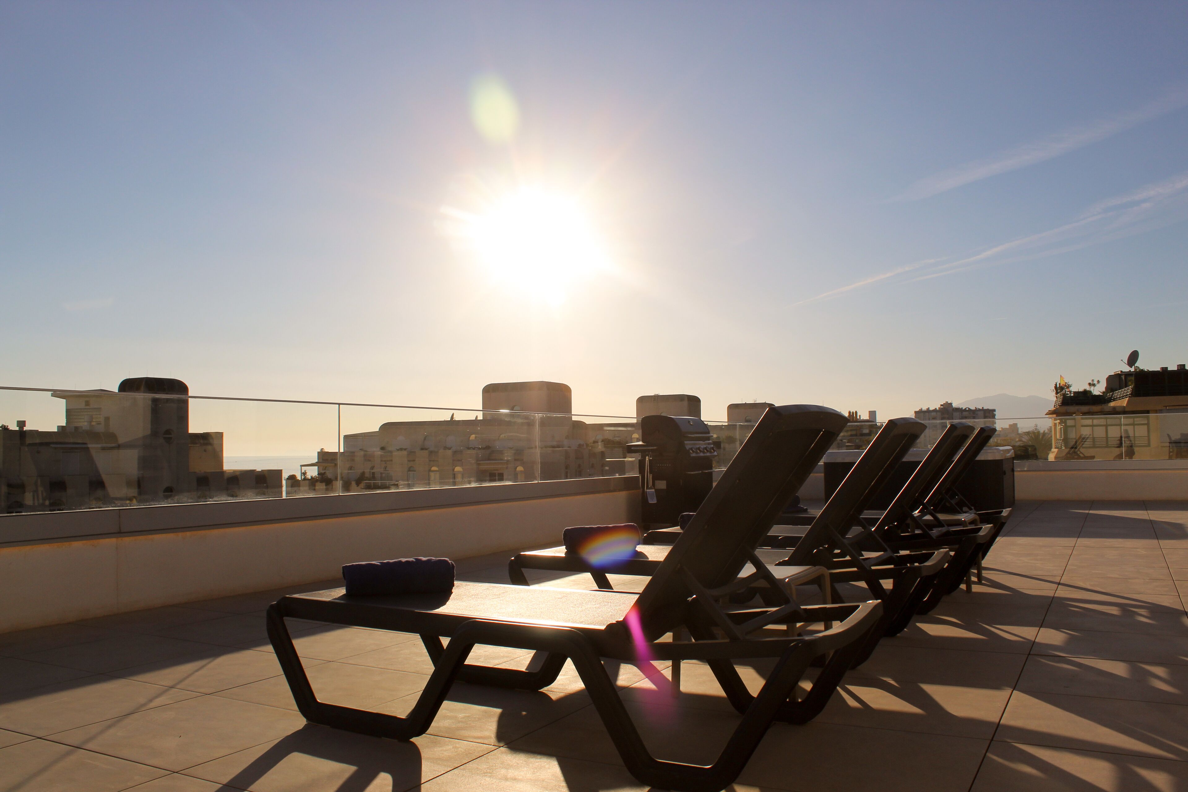 A rooftop terrace with sun loungers and a clear view of the city skyline.