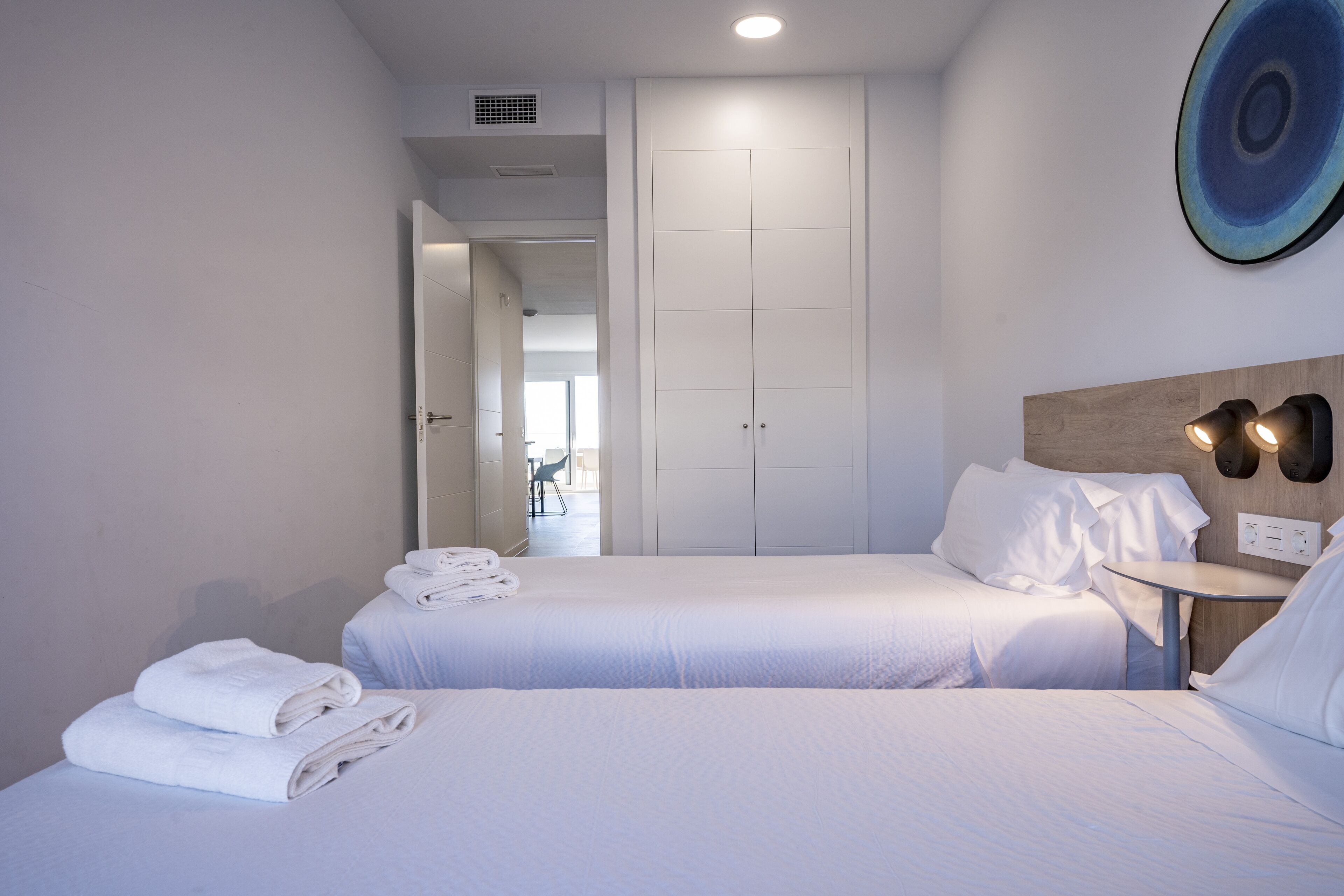 Une chambre d’hôtel avec deux lits, une petite table ronde et un luminaire fixé au mur.