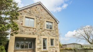 A two-story stone house with a gabled roof, large windows, and a paved driveway. - Ridley Lodge (Morpeth)