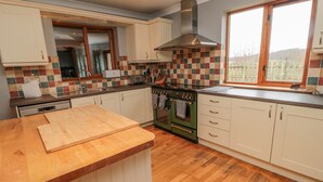 A kitchen with wooden flooring, white cabinets, a large window, and a built-in oven. - Ridley Lodge (Morpeth)