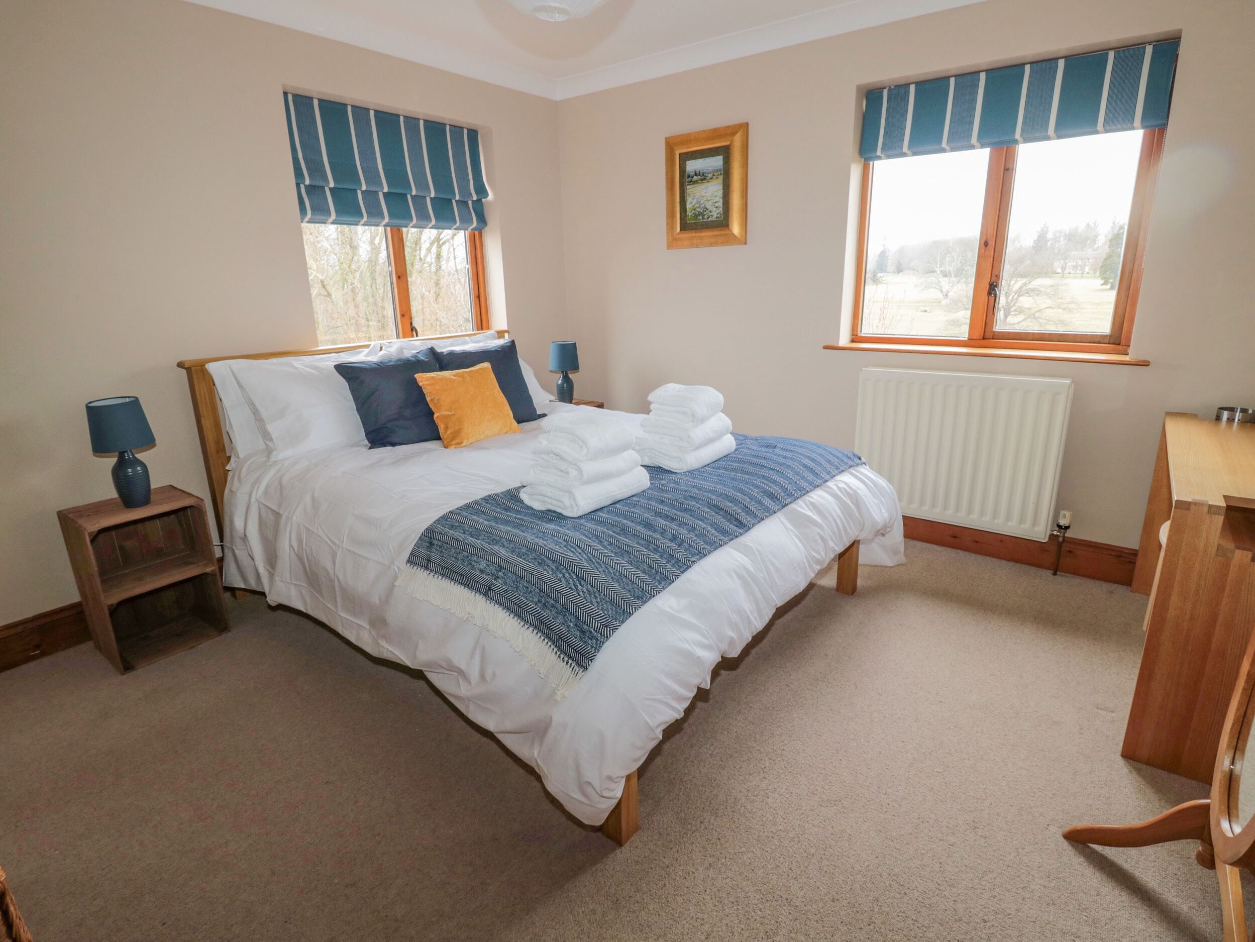 A neatly made bed with a blue and white striped blanket, a wooden headboard, and a small bedside table with a lamp.