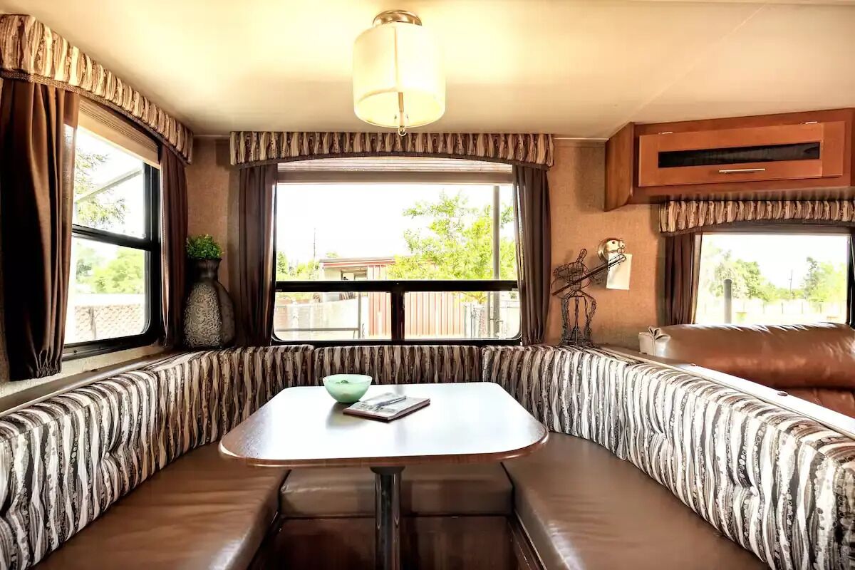 A cozy RV interior with a dining area, cushioned seating, and large windows.
