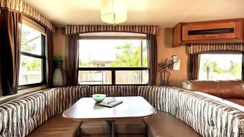 A cozy RV interior with a dining area, cushioned seating, and large windows.