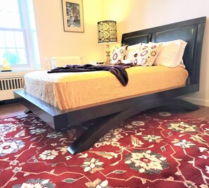 Ein Bett mit dunklem Kopfteil, einer gemusterten Tagesdecke und dekorativen Kissen.