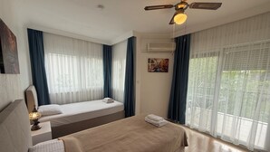 A hotel room with two beds, a ceiling fan, an air conditioning unit, and large windows with curtains. - Arslan Villa (Marmaris)