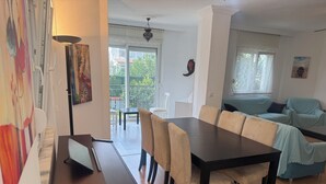 A dining area with a long table and chairs, a sofa, and a balcony with a view of greenery. - Arslan Villa (Marmaris)