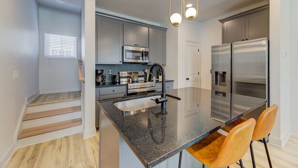 A modern kitchen with granite countertops, stainless steel appliances, and a central island with bar stools. - Green House @ Township - Unit B | 3BR 3BA (Columbia)