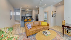 A modern living room with a brown leather sofa, a coffee table, and a colorful rug. - Green House @ Township - Unit B | 3BR 3BA (Columbia)
