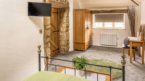 Habitación con pared de piedra, armario de madera, televisor, radiador, ventana con persianas y una planta.