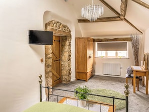A room with a stone wall, a wooden wardrobe, a television, a radiator, a window with blinds, and a plant.