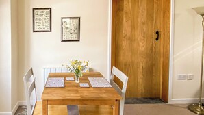 Een eethoek met een houten tafel, witte stoelen en een vaas met bloemen. Twee ingelijste foto's hangen aan de muur.