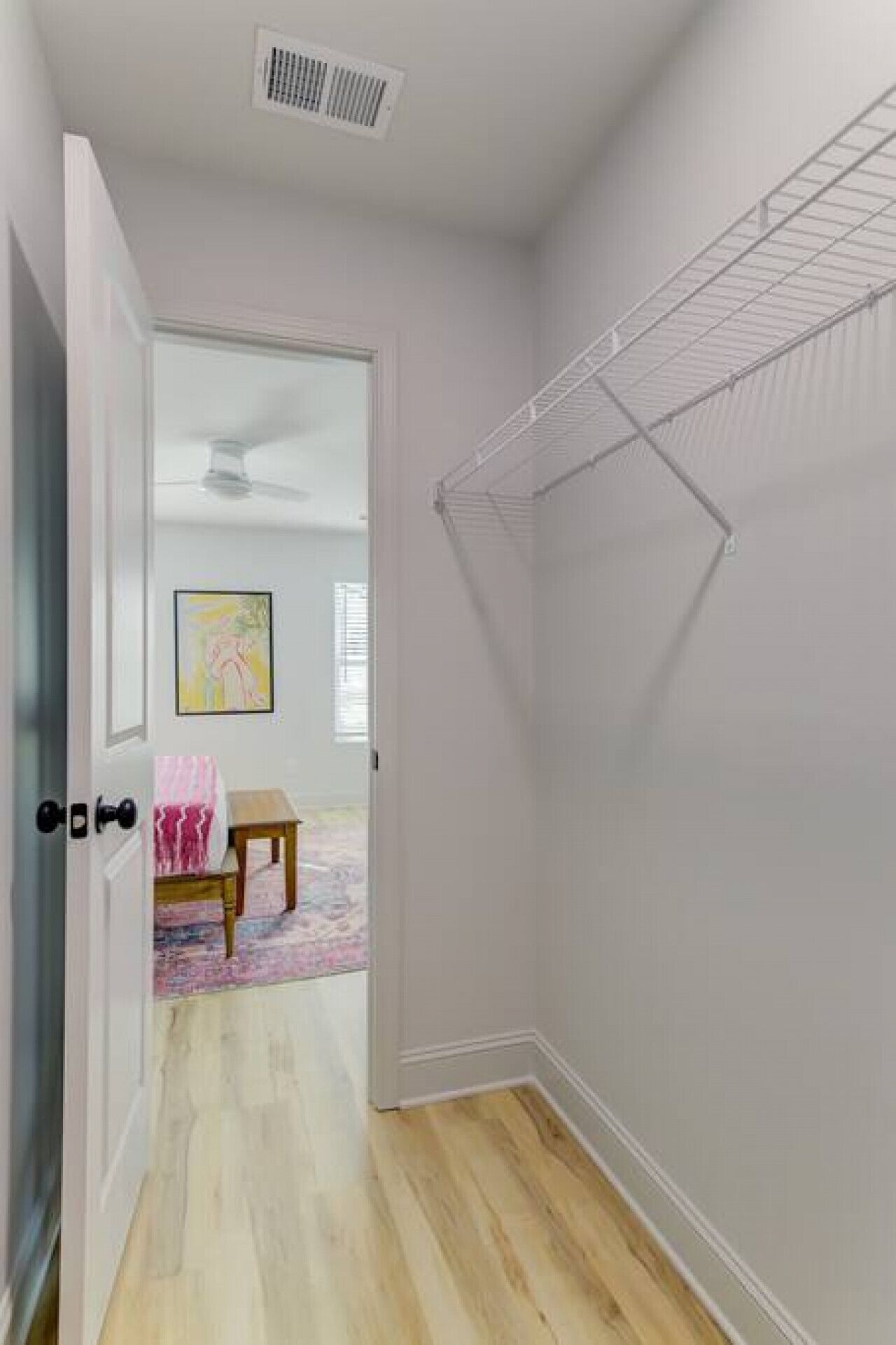 A walk-in closet with a metal shelving unit, a door with a keyhole, and a small table with a pink rug.