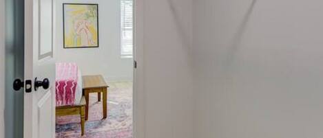 A walk-in closet with a metal shelving unit, a door with a keyhole, and a small table with a pink rug.
