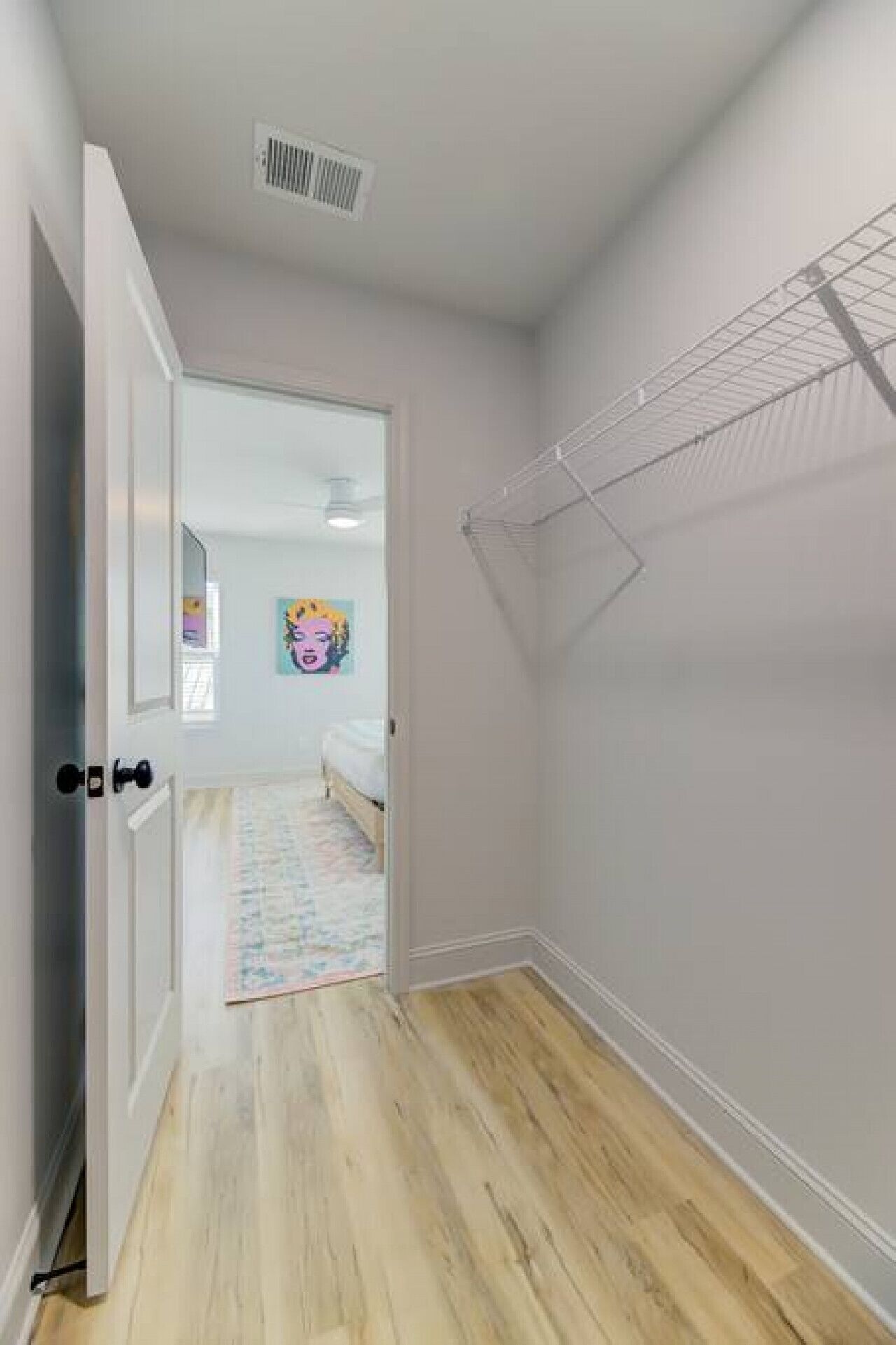 Un couloir avec un plancher en bois, une porte blanche et une bouche d’aération au plafond.