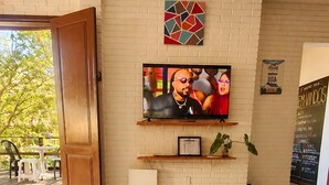 A living room with a TV mounted on a brick wall, a sofa, and a door leading outside. - 5to Elemento House (Búzios)