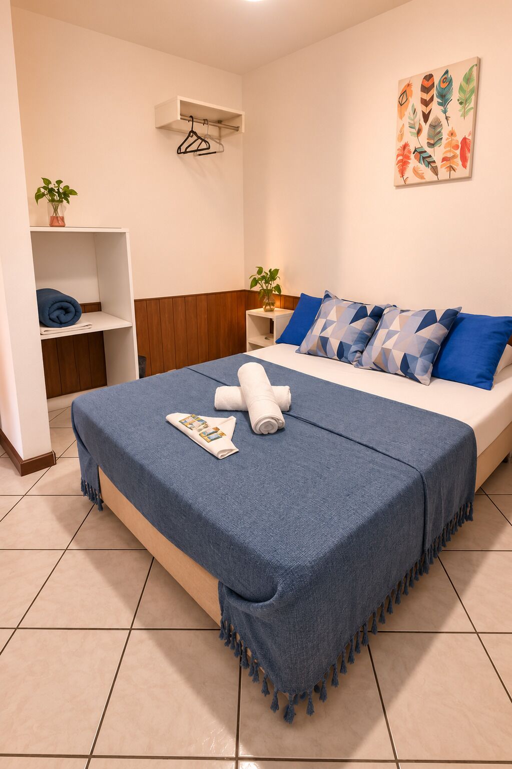 A hotel room with a bed, a side table, a shelf with a plant, and a wall-mounted air conditioner.