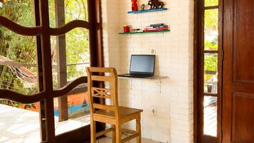 Une pièce avec une chaise en bois, un ordinateur portable posé sur une étagère et un mur en briques blanches.