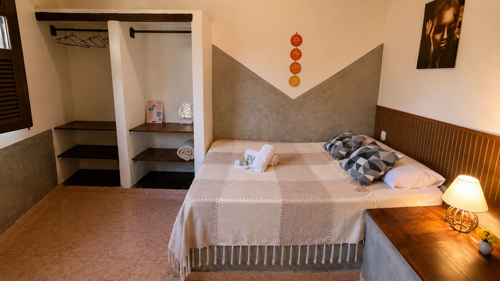 Un dormitori amb un llit, una tauleta de nit, una làmpada, una paret amb un disseny geomètric i una escala que condueix a un armari.