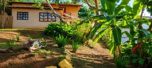 A house with a tiled roof, a balcony, and a garden with various plants and a wooden fence. - 5to Elemento House (Búzios)
